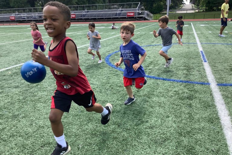 A group of young boys running on a turf field during a sports day camp program