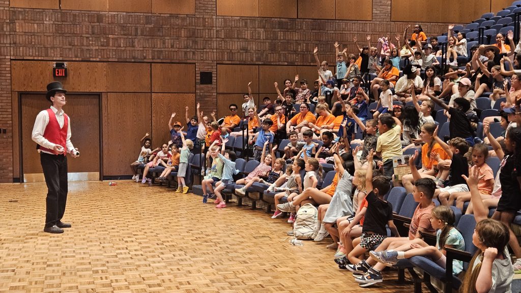 a magician performing in front of a crowd of summer day camp campers 