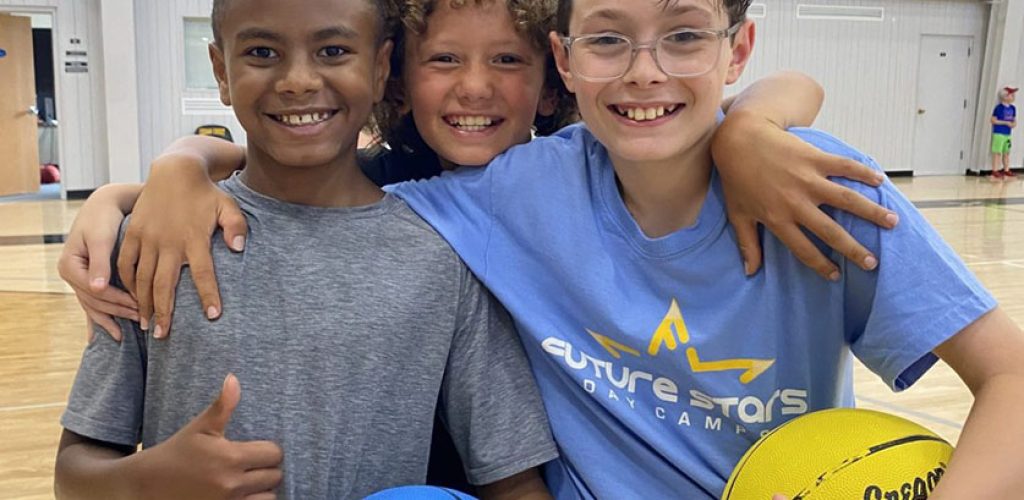 A group of three boys smiling confidently during an All Sports program at day camp